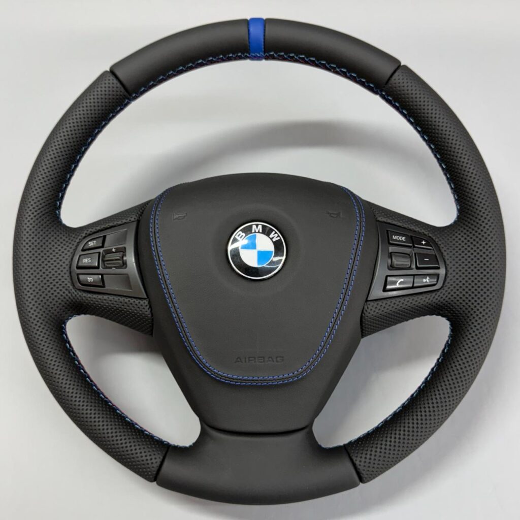 Volan BMW retapițat în piele neagră perforată, cu cusătură și marcaj central albastru